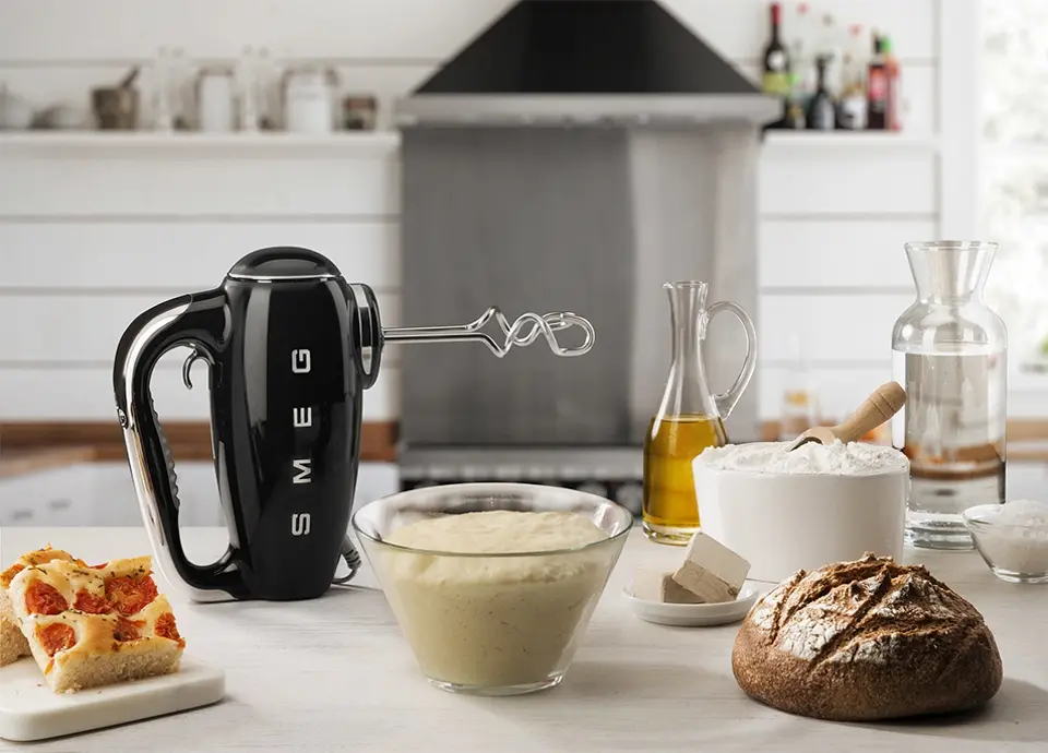 Czarny mikser ręczny SMEG w stylu retro na tle kuchni z dodatkami do pieczenia